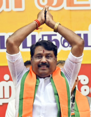 Nainar Nagendran with both hands raised above his head in greeting, wearing a party shawl, before a crowd