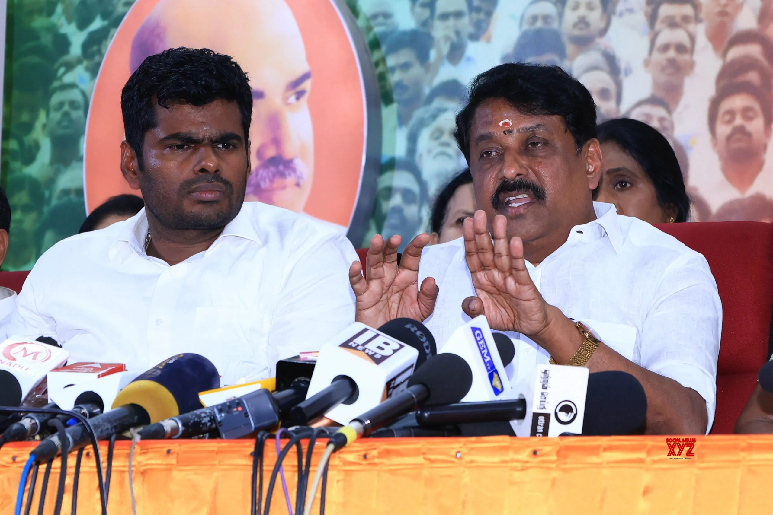 Nainar Nagendran speaking at a press conference table crowded with television microphones, with K. Annamalai seated beside him