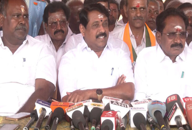 Nainar Nagendran seated at a press meeting with colleagues on either side, speaking to a table full of television microphones