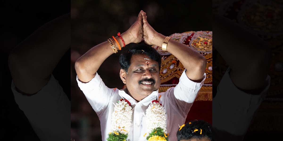 Nainar Nagendran at a night-time public event, wearing flower garlands and raising both hands together in greeting