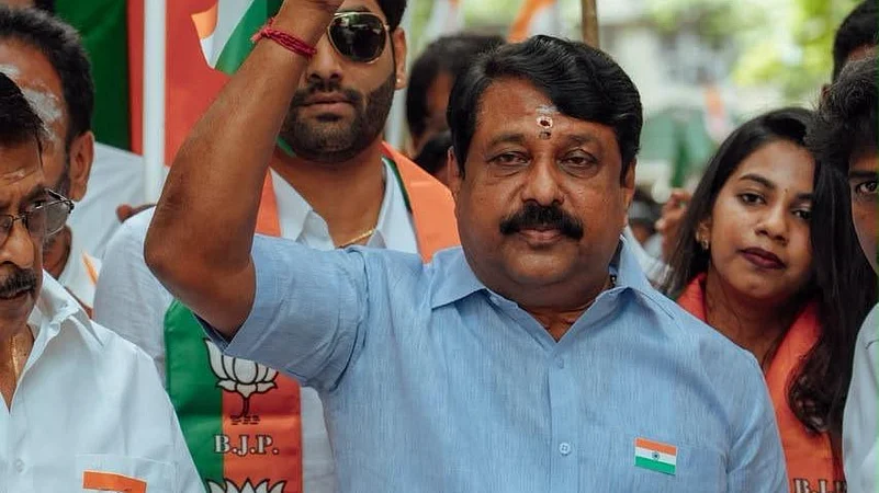 Nainar Nagendran raising a clenched fist while walking in a procession, wearing a light blue shirt with a small Indian flag badge, surrounded by party supporters