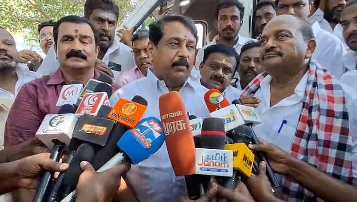 Nainar Nagendran surrounded by supporters, speaking into a dense bank of Tamil television news microphones held up in front of him